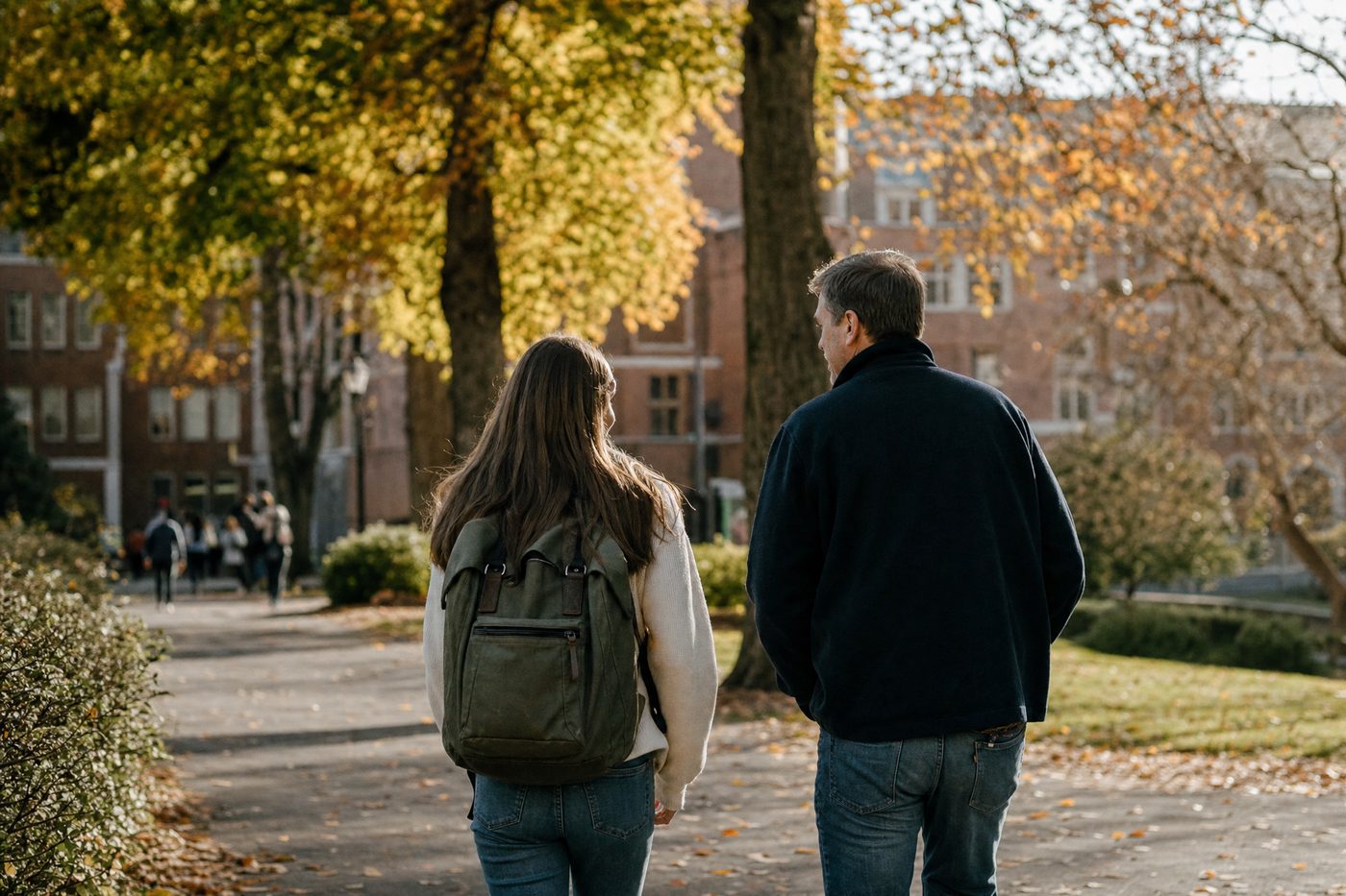 A father and his teenage daughter walking a leafy college campus path in autumn, seen from behind