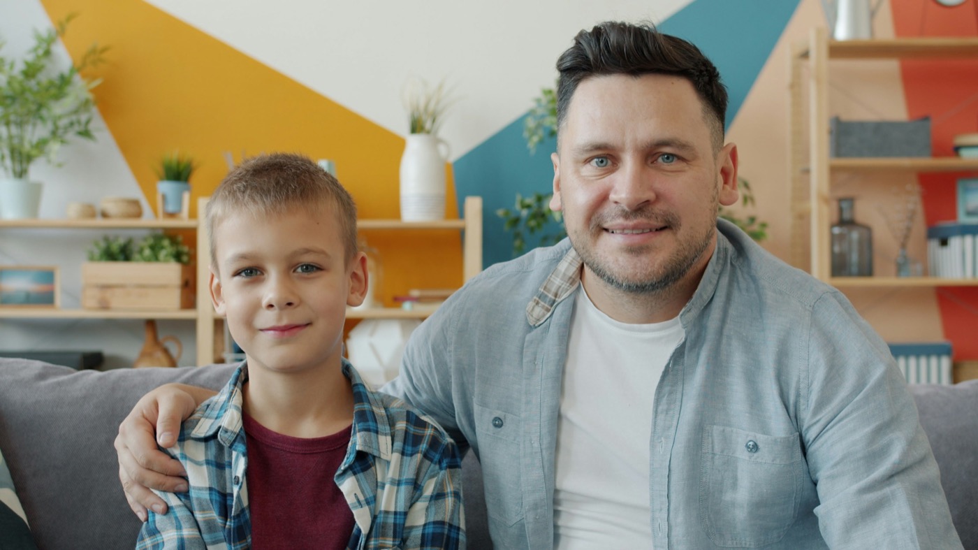 A dad sitting on a couch with his school-age son